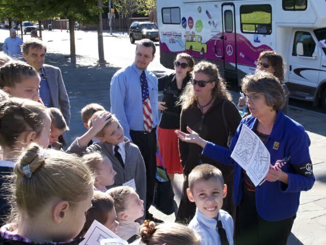 Mary Beth Tinker talking with a group of youth and adults. A mobile home with peace symbol painted on the side is in the background.
