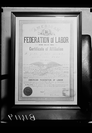 Printed document in frame with the text, 'American Federation of Labor Certificate of the Affiliation,' in large black font. Watermark of Eagle and pressed seal in lower left corner.